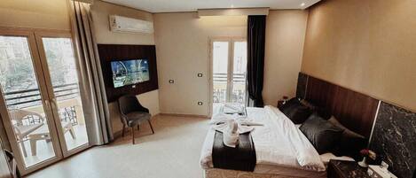 Ein modernes Hotelzimmer mit einem großen Bett, einem Flachbildfernseher, einer Sitzecke mit einem Sessel und einem Balkon mit Blick.