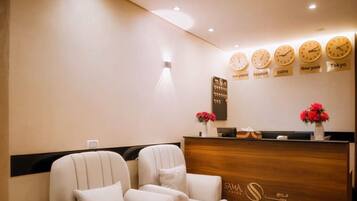 A reception area with a wooden desk, two white armchairs, a small table with a vase of flowers, and wall clocks displaying different time zones.