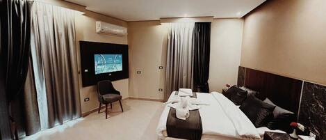 A modern hotel room with a large bed, a TV mounted on the wall, and a desk with a chair.