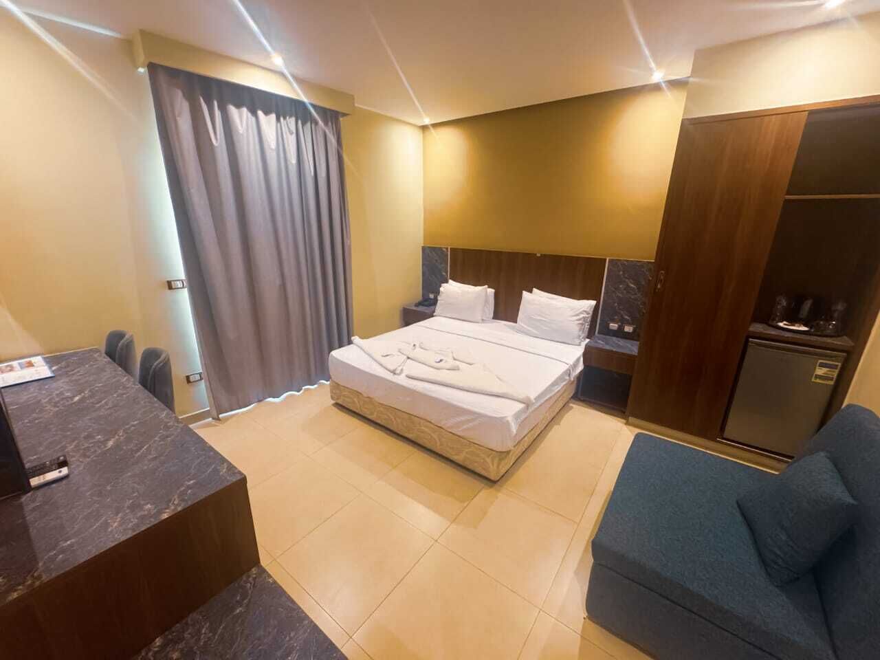 Quarto de hotel com cama, escrivaninha, cadeira, guarda-roupa e minibar.