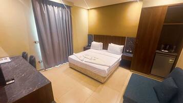 Quarto de hotel com cama, escrivaninha, cadeira, guarda-roupa e minibar.