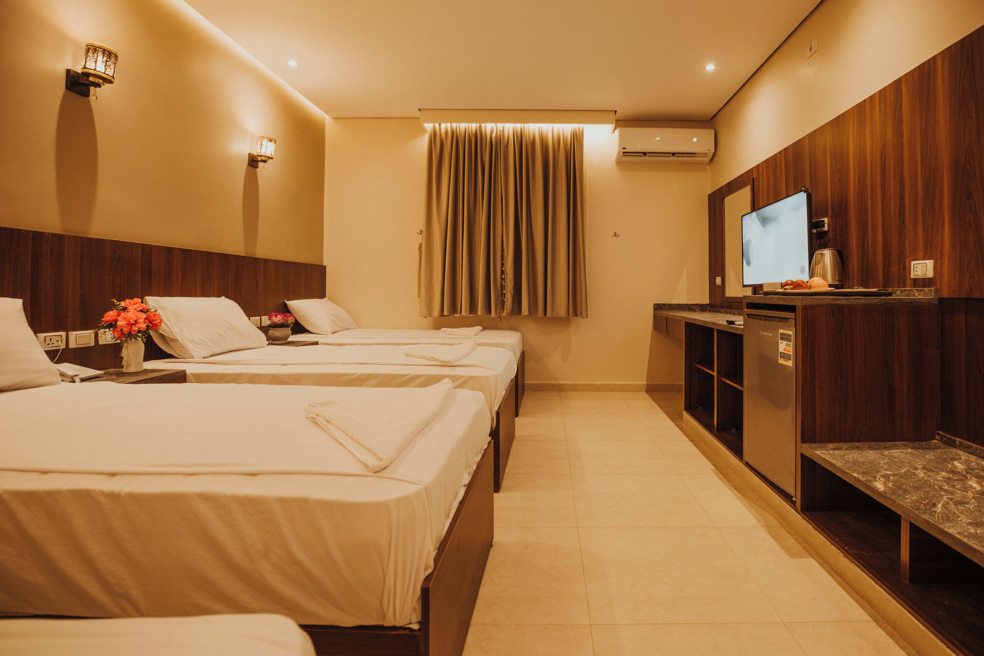 Une chambre d’hôtel avec trois lits, une télévision, un minibar et un mur recouvert de panneaux de bois.