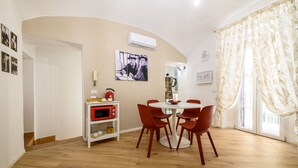 A dining area with a round table, red chairs, a white shelf with a red microwave, and a wall-mounted air conditioner. - Vico Graziella 12 in Naples (Naples)