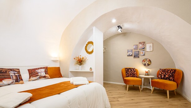 A hotel room with a large bed, two orange armchairs, a small table, and a wall with framed pictures. - Vico Graziella 12 in Naples (Naples)