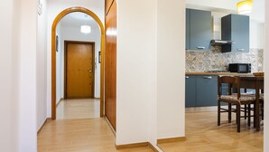 Corredor que dá para uma cozinha com micro-ondas, porta de madeira e painel decorativo.