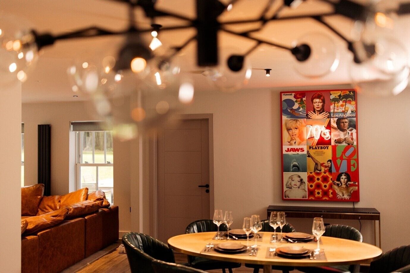 A dining area with a round table set for four, a sofa with orange cushions, and a poster on the wall.