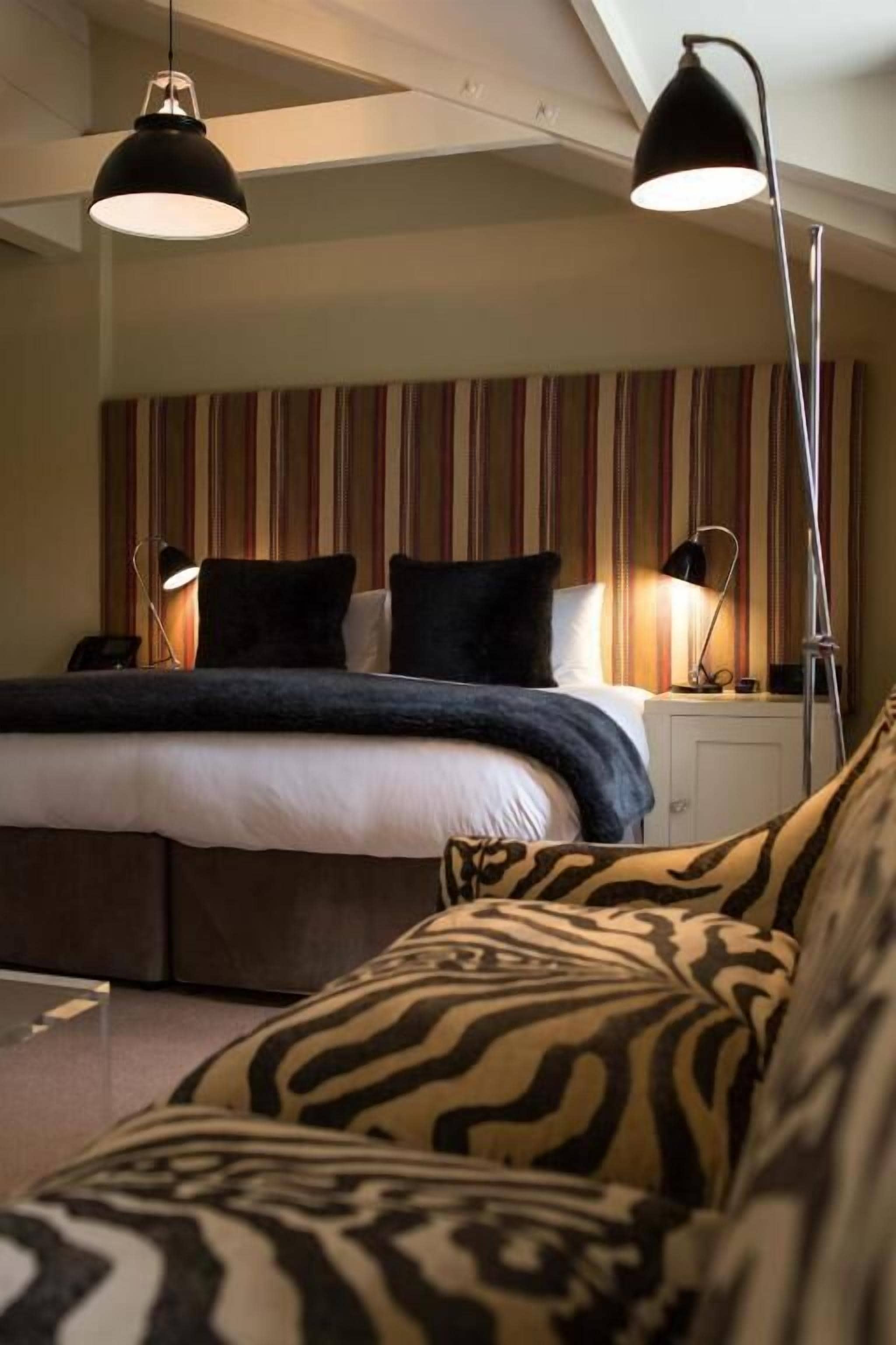 Een hotelkamer met een bed, gestreepte gordijnen, een sofa met zebraprint en twee hanglampen.