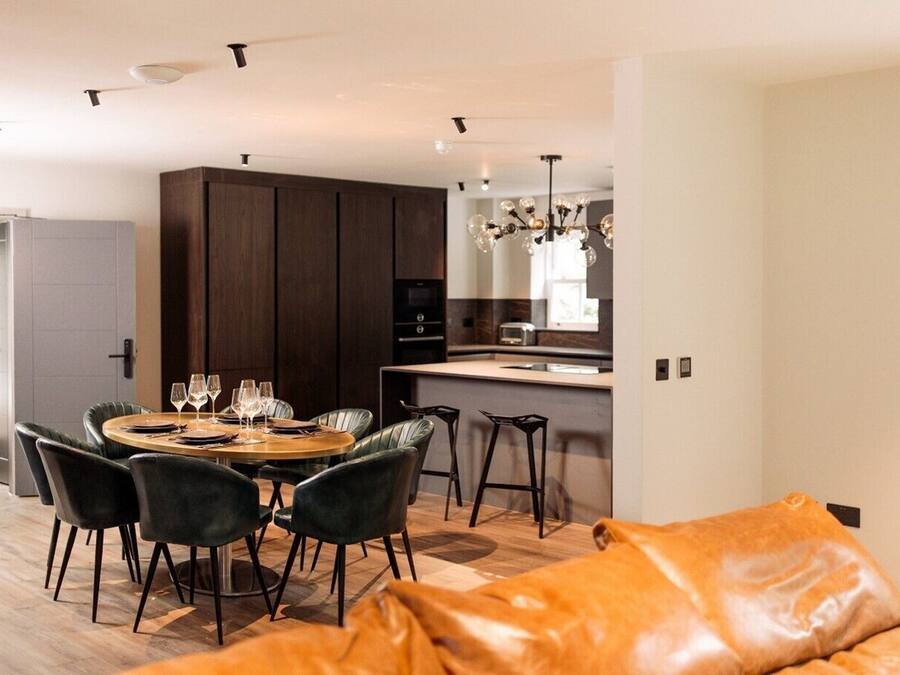 A modern kitchen with dark wood cabinets, a dining area with a round table and chairs, and a leather sofa in the foreground.