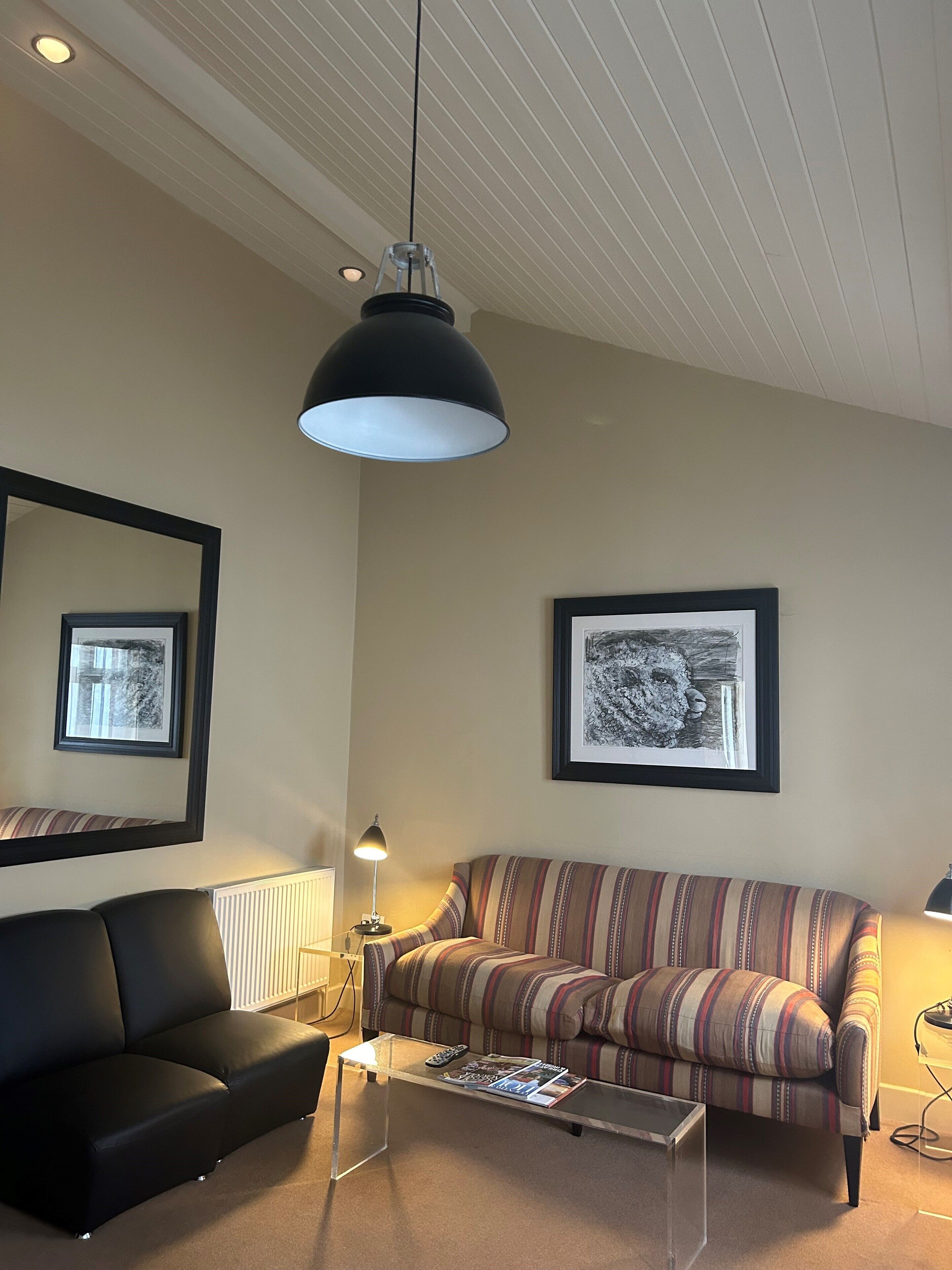 Een woonkamer met een zwarte bank, een gestreepte bank, een glazen salontafel en twee ingelijste foto's aan de muur.
