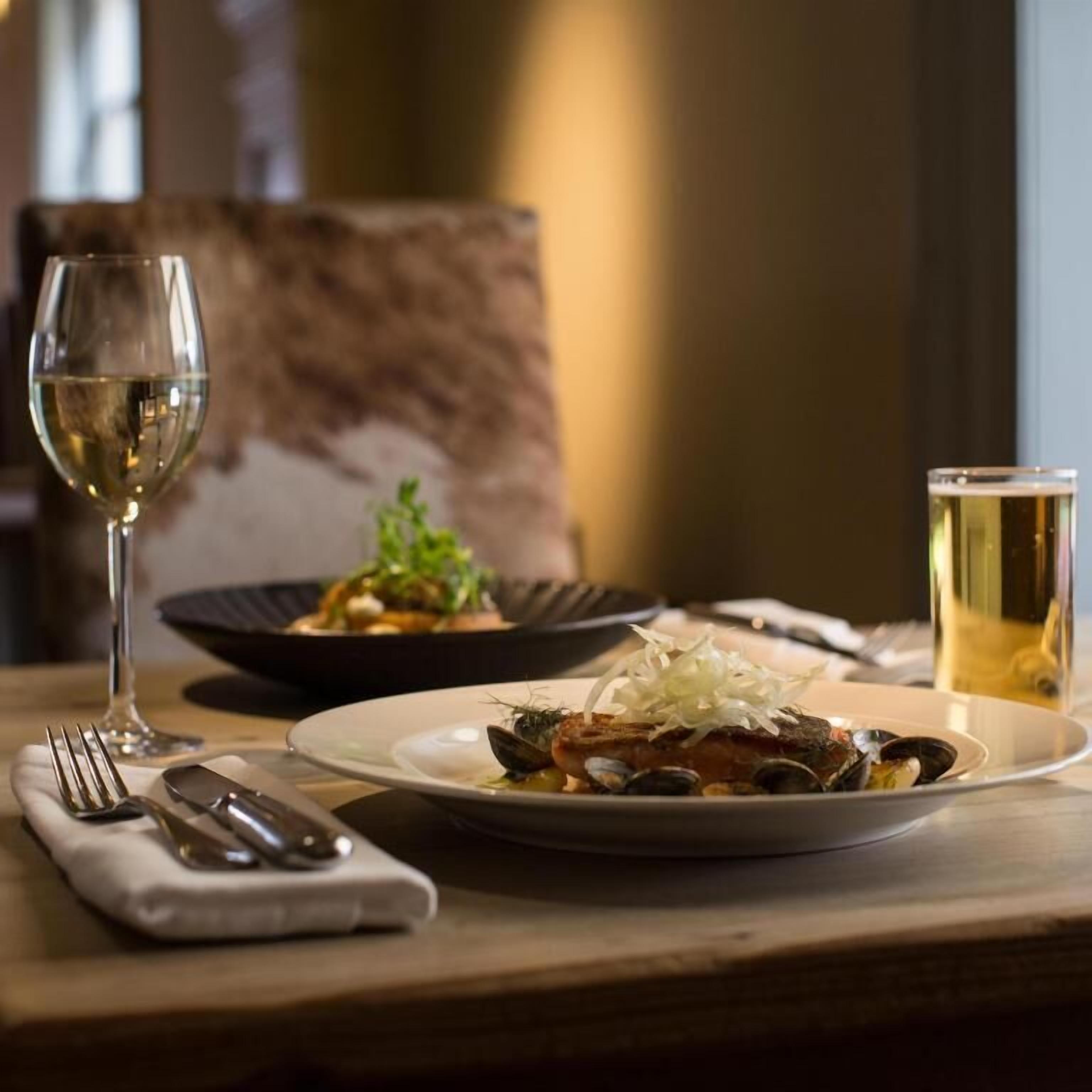 A dining table with plates of food, a wine glass, and a beer glass.