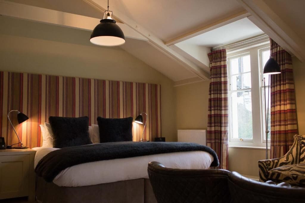 A bedroom with a bed, two bedside lamps, a window with curtains, and a chair.
