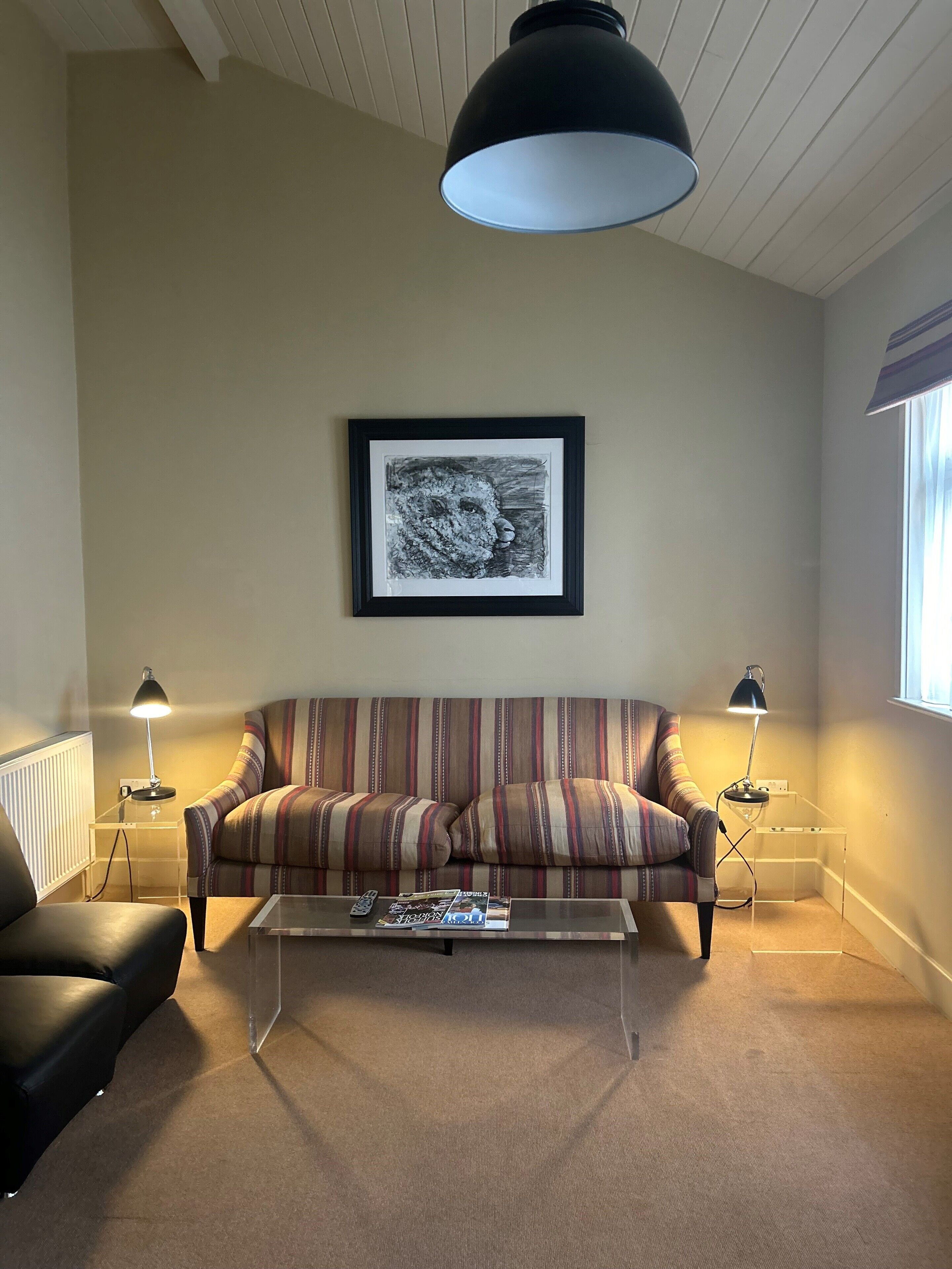 A living room with a striped sofa, a coffee table, two side tables with lamps, a framed picture on the wall, and a window with curtains.