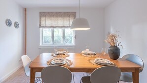 A dining room with a wooden table set for four, a hanging light fixture, and a window with a patterned valance.