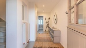 A narrow hallway with a radiator, a small table with a cup, and a window on the right.