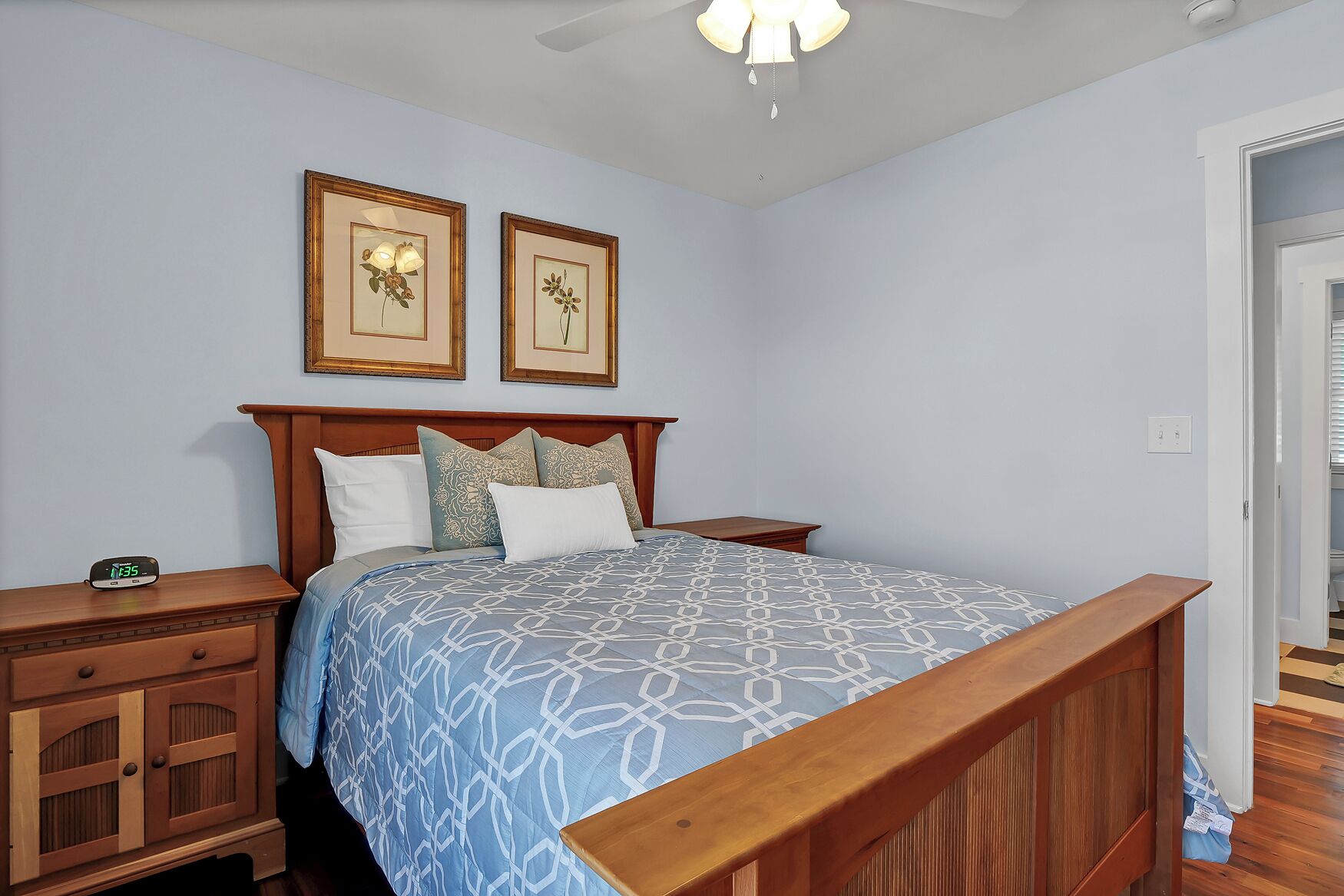 Quarto com estrutura de cama de madeira, mesa de cabeceira com relógio e duas quadros pendurados na parede.