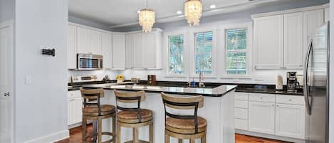 A modern kitchen with white cabinetry, a central island with bar stools, a stainless steel refrigerator, and pendant lighting.