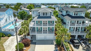 A multi-story house with a large garage, surrounded by palm trees and other residential buildings. - Searenity | 5BR Marshview Retreat w/ Game Room, Elevator & Close to Beach (Wrightsville Beach)