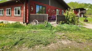 Een blokhut met veranda, een kruiwagen en een kleine tuin.