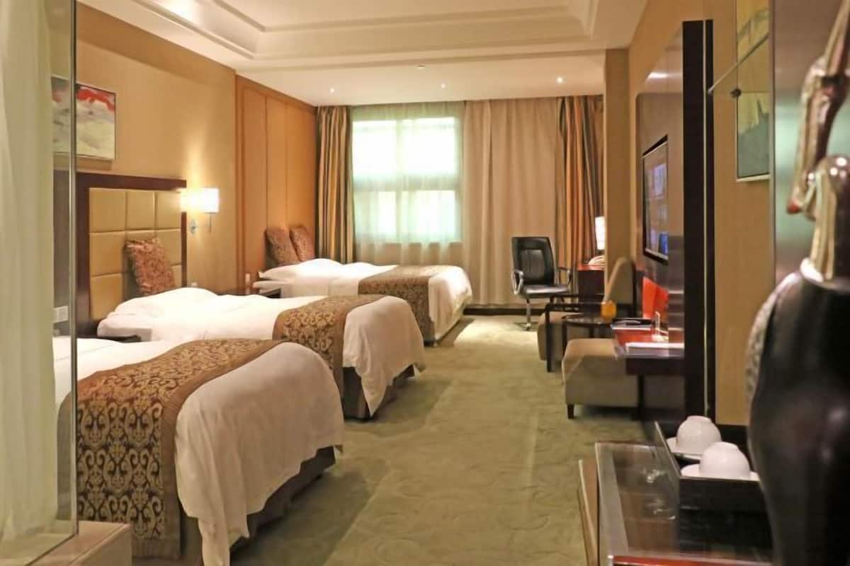 A hotel room with three beds, a desk with a computer, a TV, and a decorative vase.