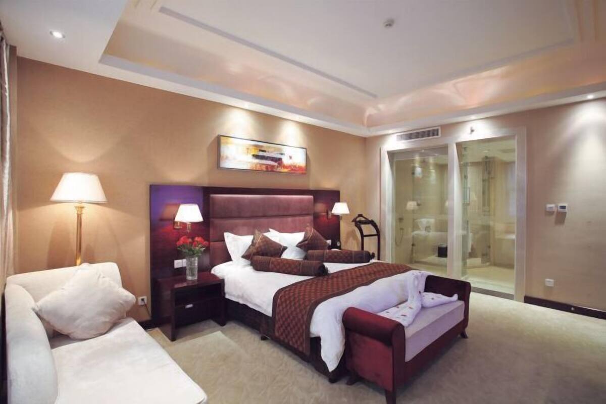 Ein Hotelzimmer mit Bett, Nachttischen, einem Sessel, einer Couch und einer Glasdusche.