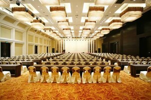 A large conference room with rows of tables and chairs, a patterned carpet, and a high ceiling with lighting fixtures.