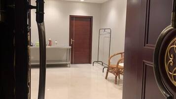 Quarto de hotel com porta de madeira, mesa branca e uma cadeira, além de um espelho.