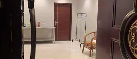A hotel room with a wooden door, a white table with a chair, and a mirror.