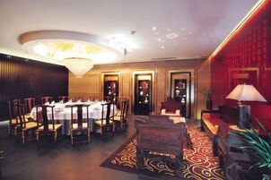 A dining area with a round table set for multiple guests, a chandelier, and a red accent wall.