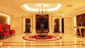 A lobby with a central ornate table, red seating, and a chandelier.
