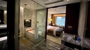A modern hotel room with a glass-enclosed shower, a bathtub, a bed with a large window, and a marble bathroom.