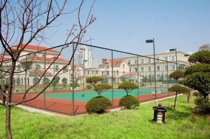 Una cancha de tenis con valla, una farola y edificios al fondo.
