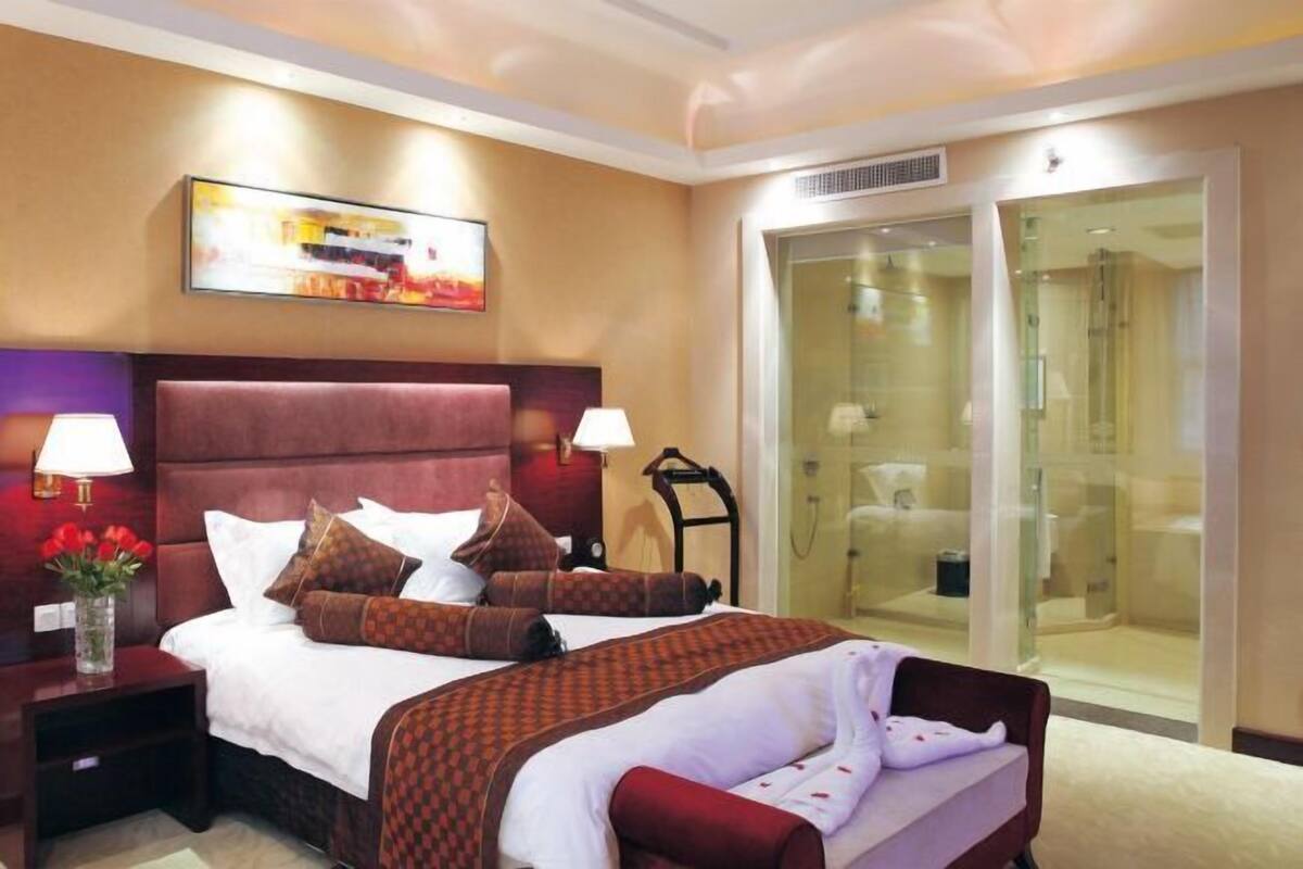 Ein Hotelzimmer mit einem großen Bett, zwei Nachttischen, einer Duschkabine aus Glas und einem Bild an der Wand.