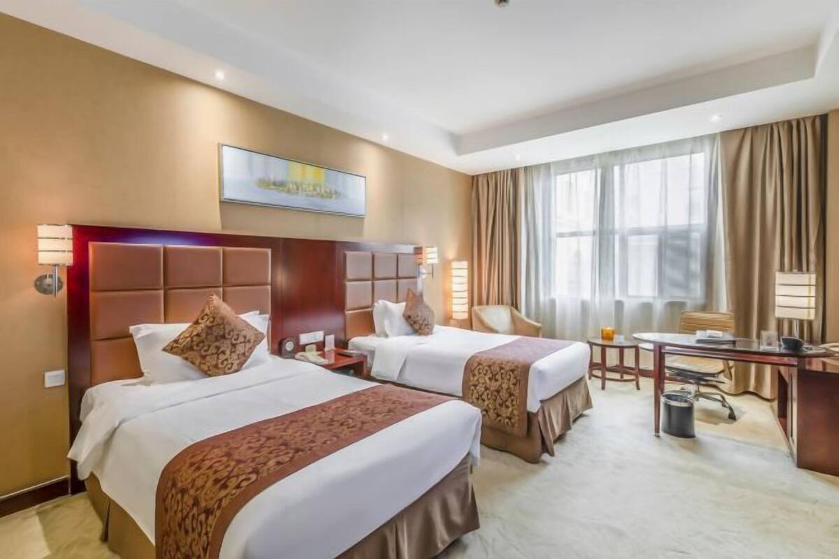 Ein Hotelzimmer mit zwei Betten, einem Schreibtisch, einem Stuhl und einem großen Fenster mit Vorhängen.