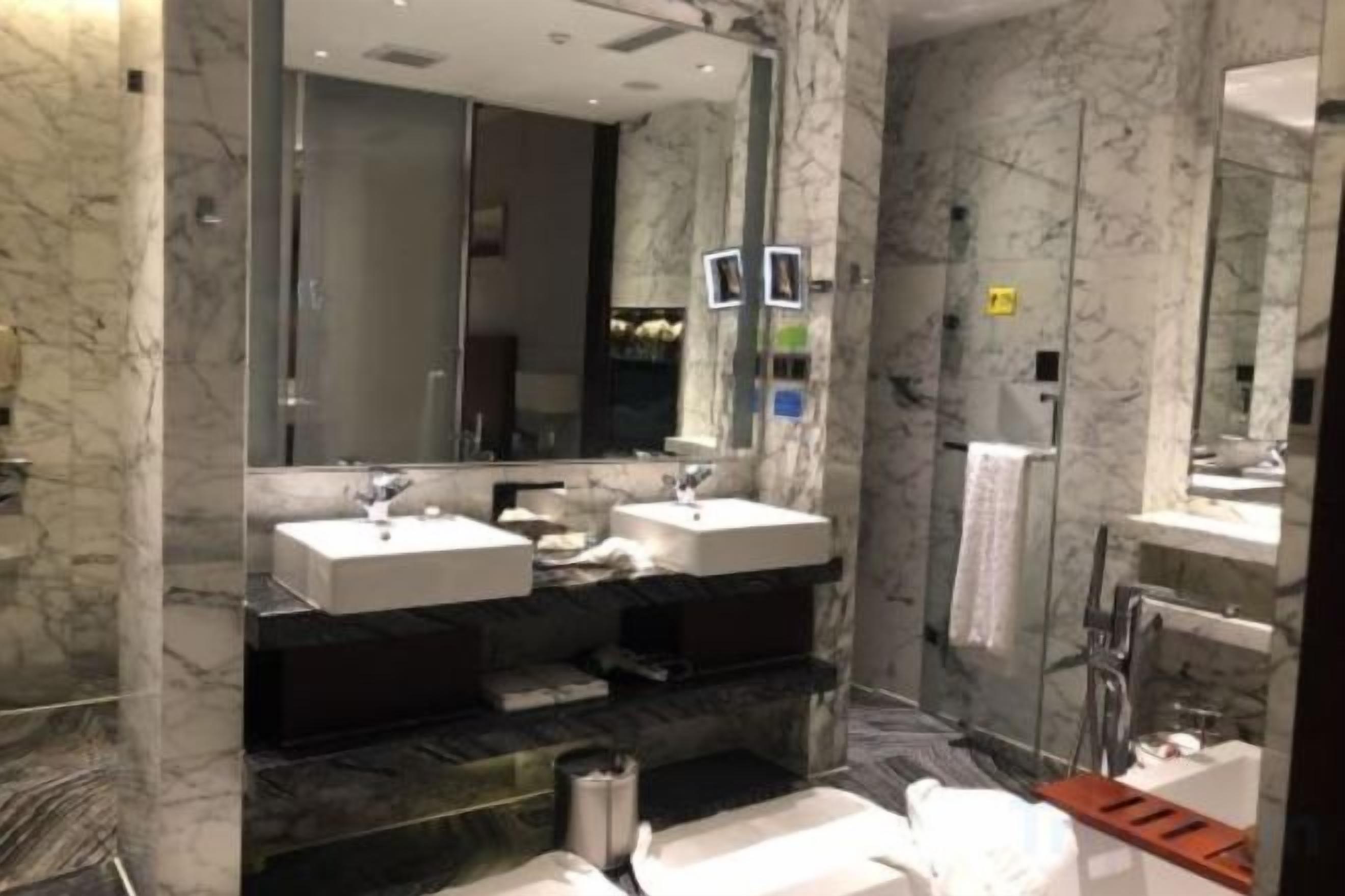 Un bagno moderno con pareti in marmo, due lavabi, uno specchio grande e una cabina doccia.