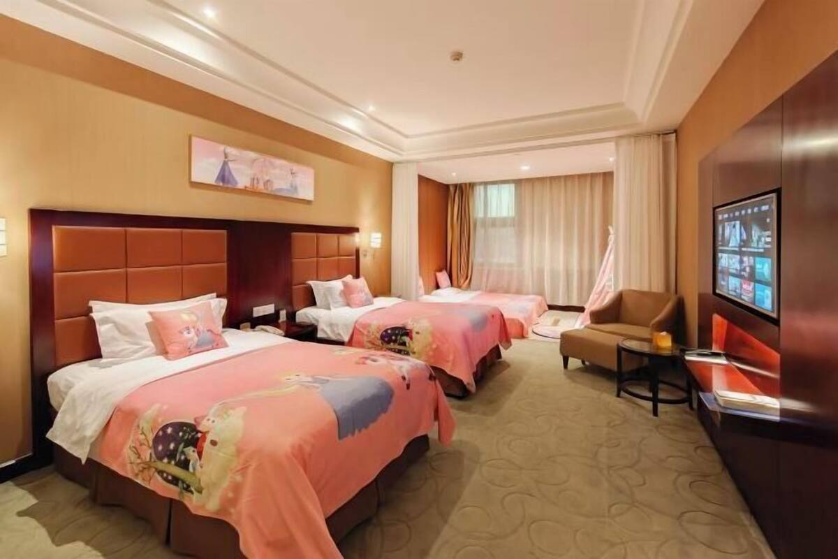 Ein Hotelzimmer mit drei Betten, einem Fernseher, einer Couch und einem kleinen Tisch.