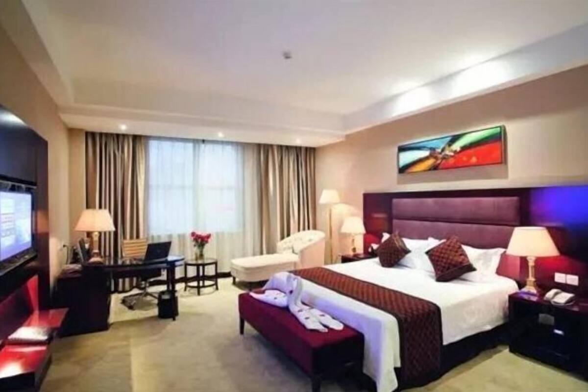 Ein Hotelzimmer mit Bett, Schreibtisch, Stuhl, Fernseher und einem Bild an der Wand.