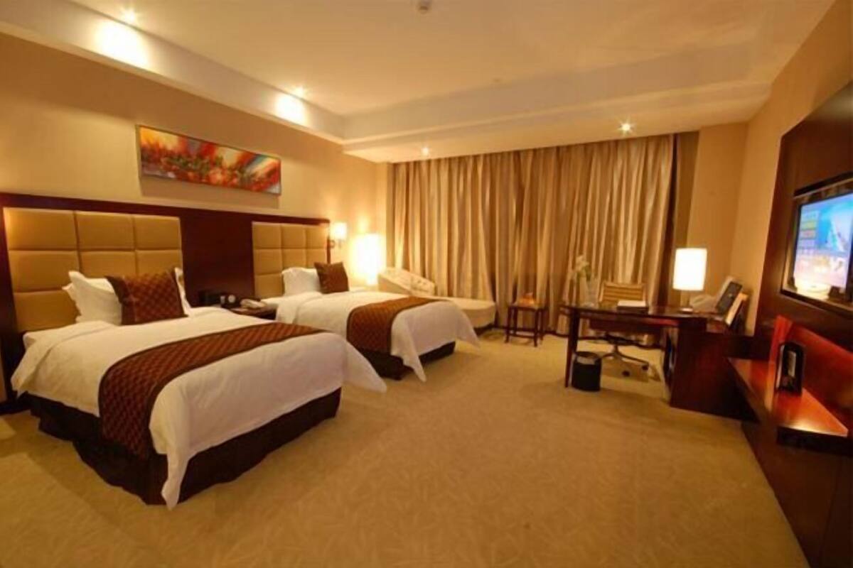 Ein Hotelzimmer mit zwei Betten, einem Schreibtisch, einem Sessel, einem Fernseher und einem großen Fenster mit Vorhängen.