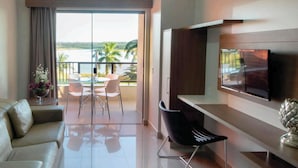 Ein modernes Wohnzimmer mit einer Couch, einem Esstisch mit Stühlen, einem Fernseher und einem Balkon mit Blick auf das Wasser und Palmen.