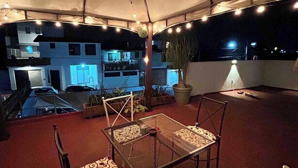 An outdoor patio area with a table and chairs, string lights, and a view of a building in the background. - Bugambilias 203 - Private Room with parking and a big terrace only for you (Santa Lucía del Camino)