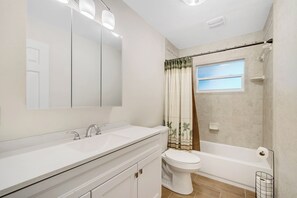 Een badkamer met een wastafelmeubel met dubbele wastafel, toilet en bad.