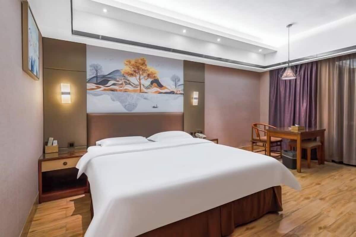 A hotel room with a bed, bedside tables, a desk, and a chair.