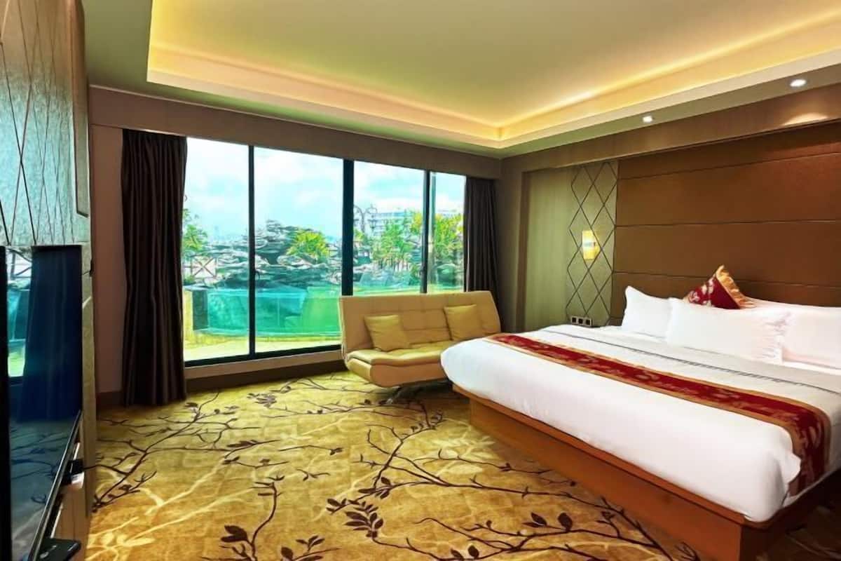 A hotel room with a large bed, a sofa, a TV, and a view of the city.