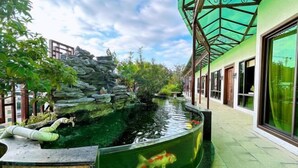 A koi pond with a curved edge, surrounded by a stone wall and greenery, adjacent to a building with large windows and a green roof. - Jinpin Feicui Hotel (Pingzhou Yuqijie Subway Station Branch Pingnan) (Foshan)