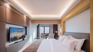 A hotel room with a large bed, a flat-screen TV mounted on the wall, a desk with a chair, and a window with curtains. - Jinpin Feicui Hotel (Pingzhou Yuqijie Subway Station Branch Pingnan) (Foshan)