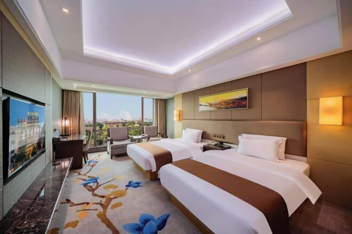 A hotel room with two beds, a desk, a chair, a TV, and a large window offering a city view.