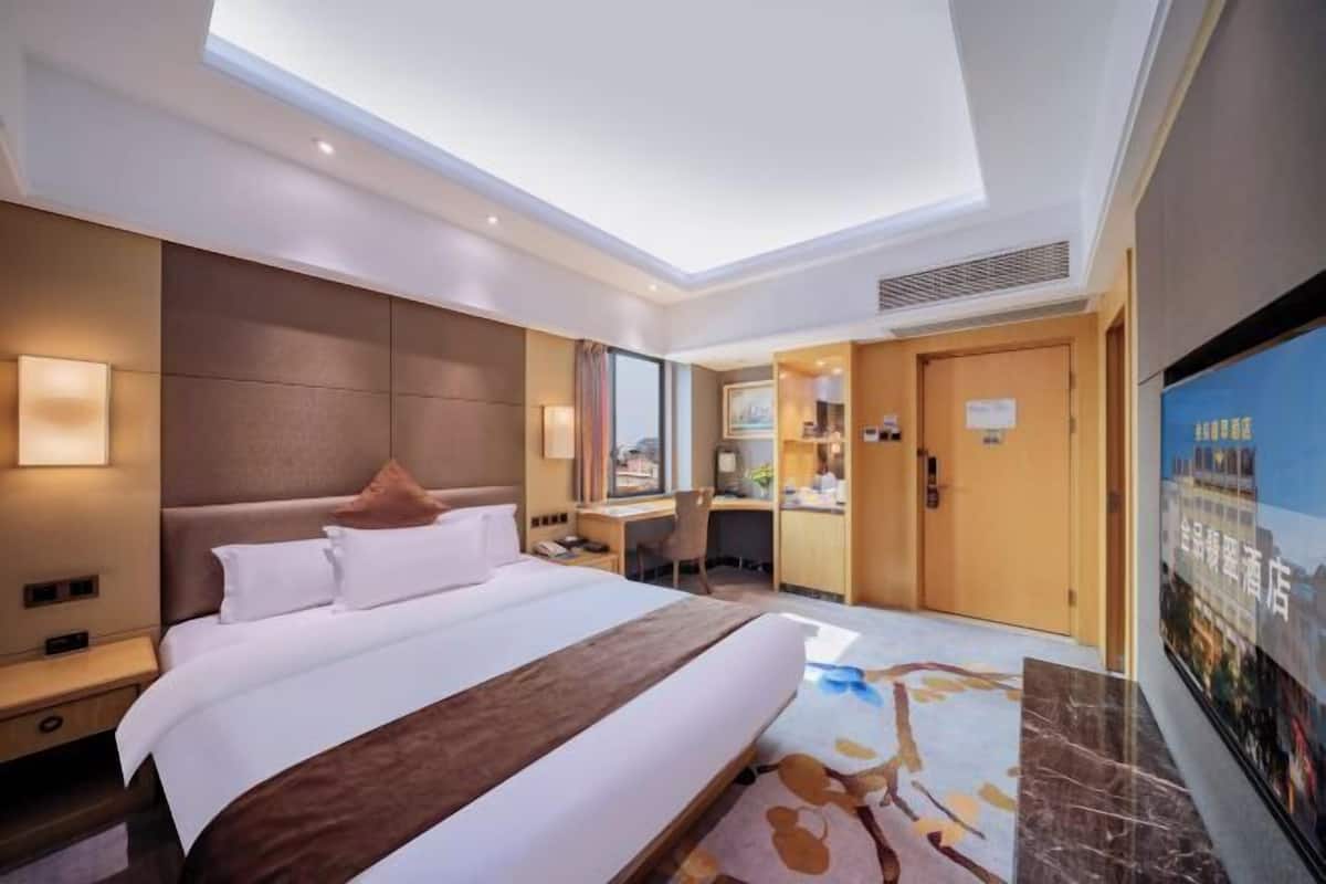 A hotel room with a large bed, a desk, a chair, and a television.