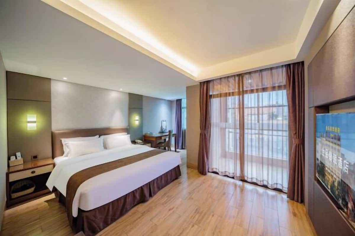 A hotel room with a large bed, bedside tables, a desk, and a large window with curtains.