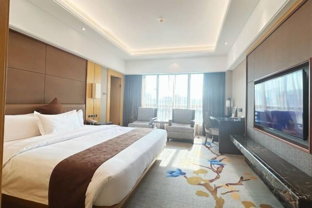 A hotel room with a large bed, a flat-screen TV, a desk, and a seating area with chairs.