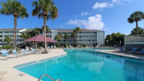 A swimming pool with lounge chairs and palm trees, surrounded by a hotel building.