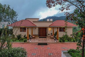 A two-story house with a red-tiled roof, a wooden door, and a front porch with chairs. - The Perfect Home Stay (Kotagiri)